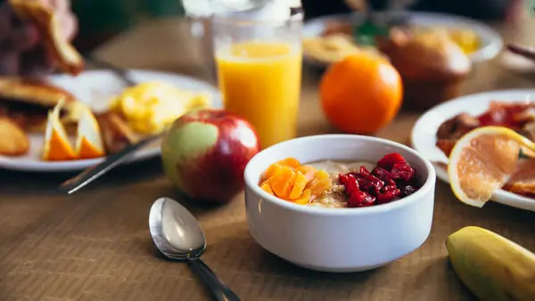 A nourishing breakfast bowl with fruit, yoghurt, and juice on a wooden table—supporting energy and sustainable wellbeing habits.
