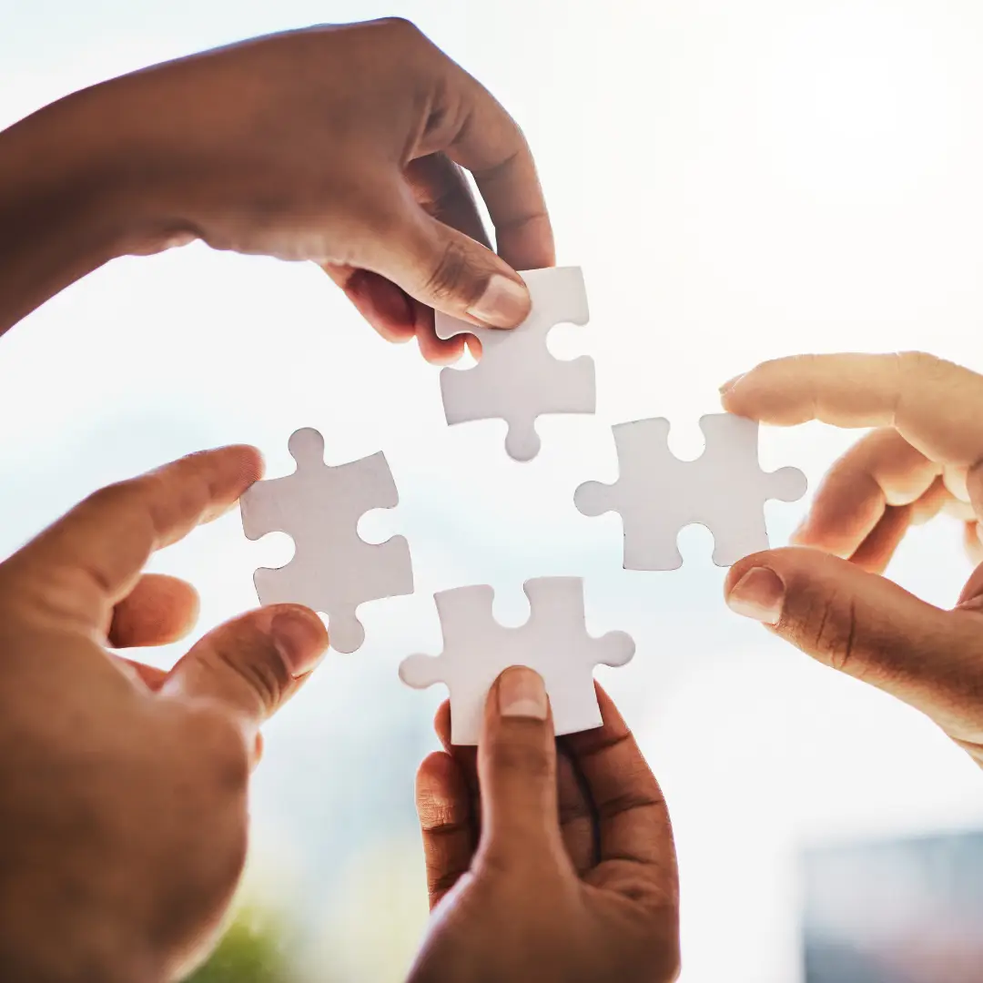 Hands connecting puzzle pieces to symbolise co-design, collaboration, and building resilient workplace wellbeing strategies.