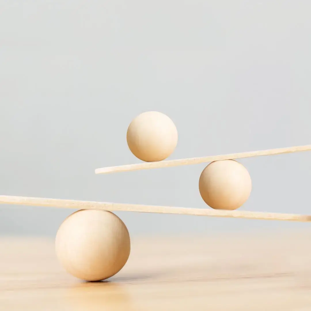 Three wooden spheres balanced on two wooden planks, symbolising balance, stability, and the foundations of thriving leadership.