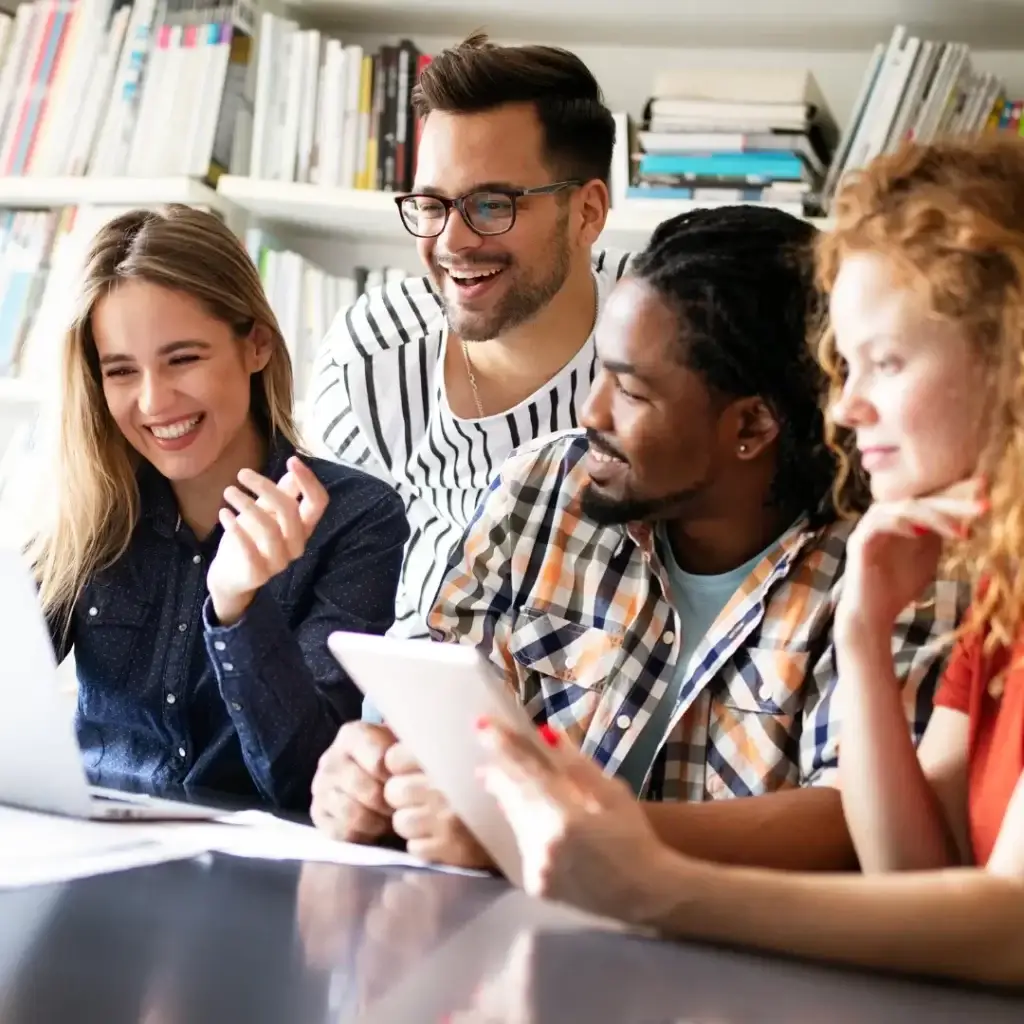 Four professionals smiling and collaborating around a laptop and tablet during a group coaching session, representing connection, growth, and learning together.