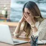 Young professional woman struggling with focus and stress, head in hands, highlighting common wellbeing challenges in modern work environments.