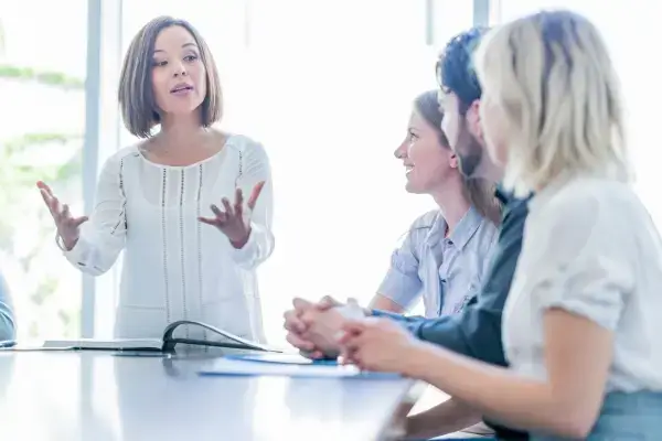 Female leader presenting confidently to colleagues in a bright modern office.
