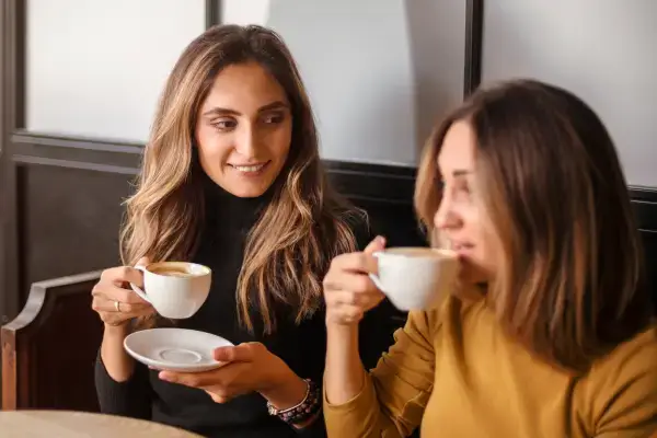Two professional women talking over coffee, representing empathy, active listening, and supportive workplace relationships.