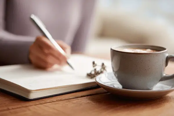 Leader journaling quietly with cup of coffee, symbolising self-reflection and intention in leadership wellbeing.